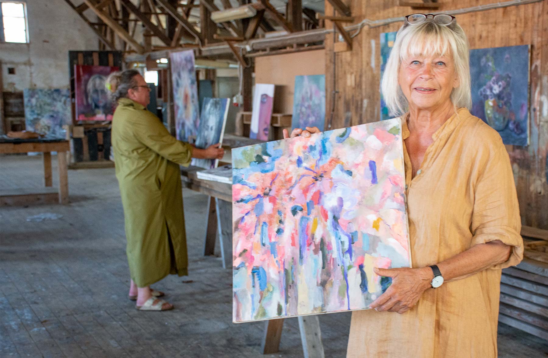 Elsebeth Hytten fremviser et af malerierne, mens Linda Hargreave i baggrunden gør overvejelser over placeringerne. Foto: Hans Jacob Sørensen.