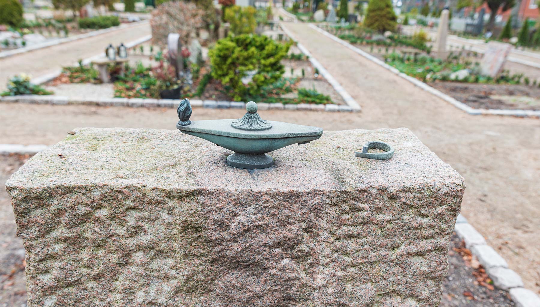 Udsmykninger på gravsteder er ofte udsat for hærværk eller tyveri, hvor figurer og som her aladdin-lamper brækkes eller sparkes af. Foto: HAS.