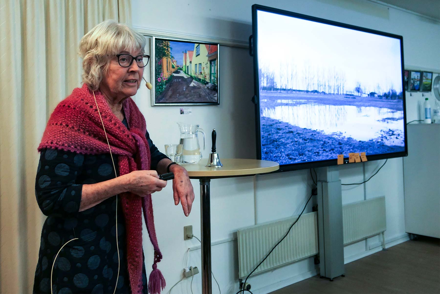 Bodil Glad viser fotos og fortæller om tilblivelsen af TAMU Storkøbenhavn. På skærmen i baggrunden ses på hendes foto, der er fra 1904, at der også dengang var temmelig meget vand på gårdens marker. Foto: Dines Bogø.